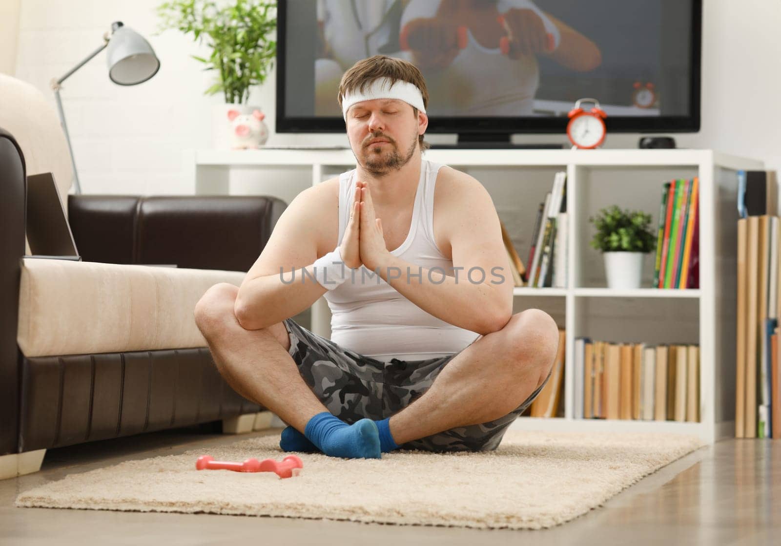 Young attractive fitness man lies on a fat mat with overweight performs stretching exercises and smiles