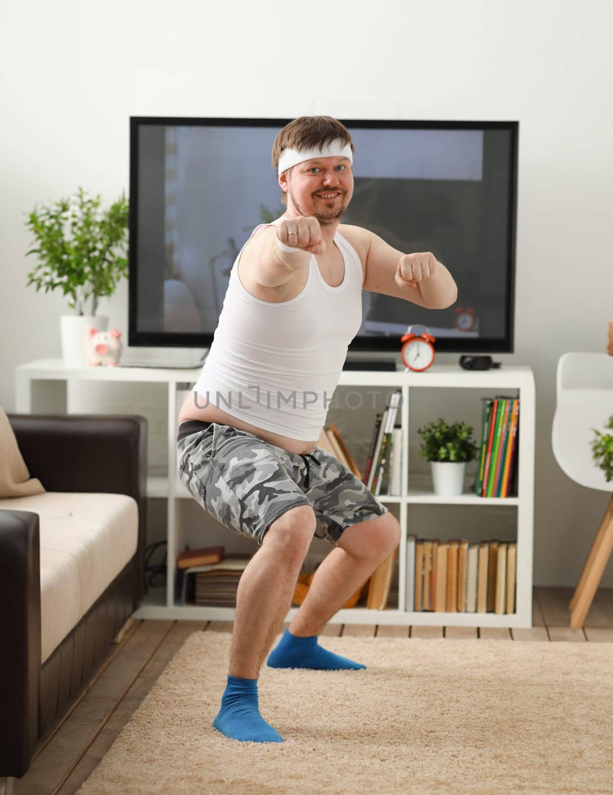 Young handsome man in shorts and vest holds pink dumbbells in hand. Watch tv lessons single combats is practicing receptions of sensei one home fitness indoor training independent education remotely