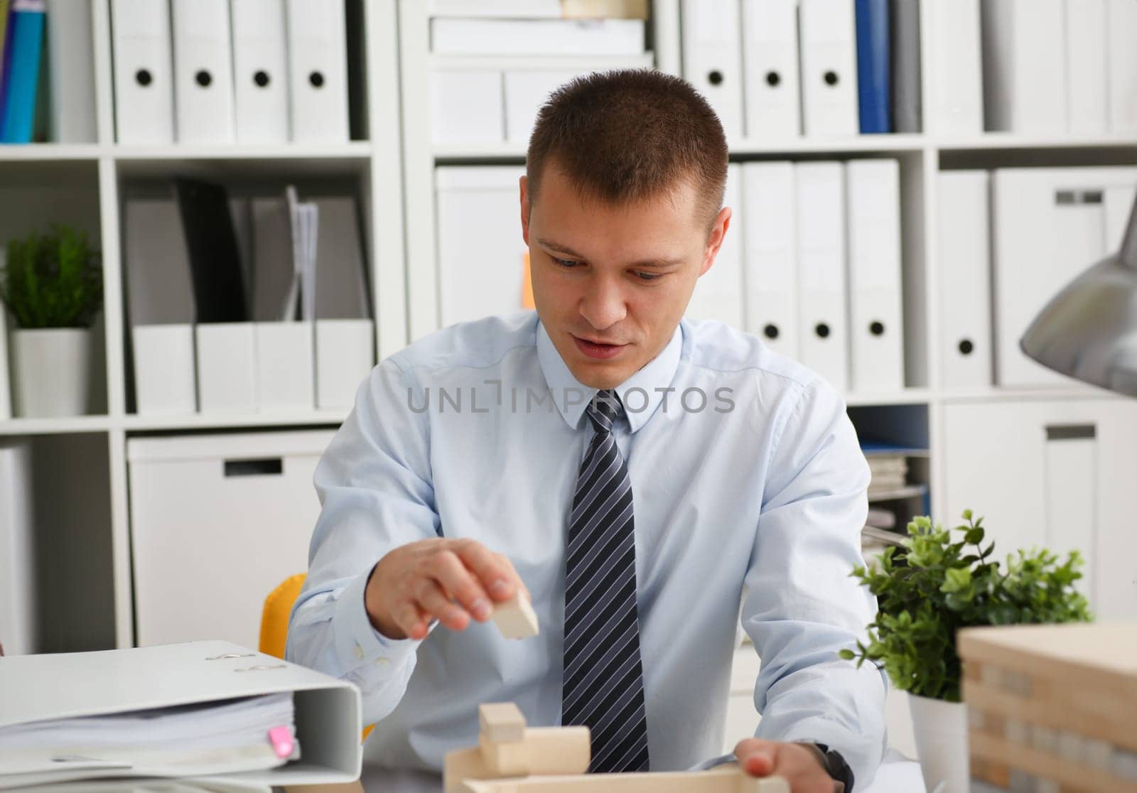 Businessman plays in strategy hand rearranging wooden blocks involved during break at work in office sitting table gaming pile fun joy pastime concept