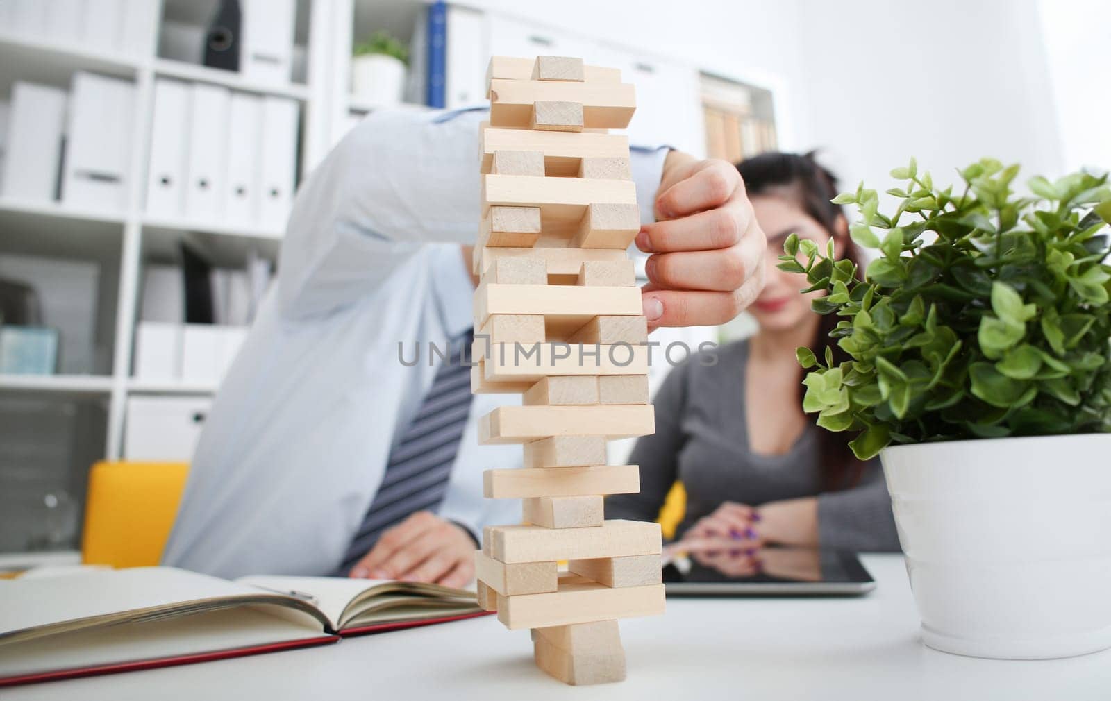 Businessman and businesswoman plays in strategy hand rearranging wooden blocks involved during break at work in office sitting table gaming pile fun joy pastime concept.