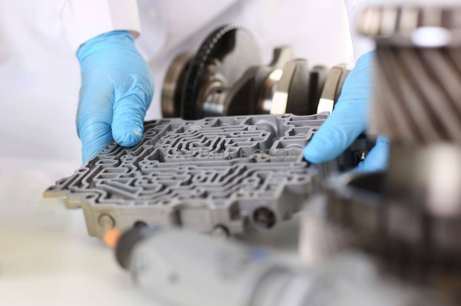 The auto repair service repairman automatic gearboxes holds in his hand in blue protective gloves. Hydroblock detail dehydrates the diagnostics and estimates the detail test transmission closeup.