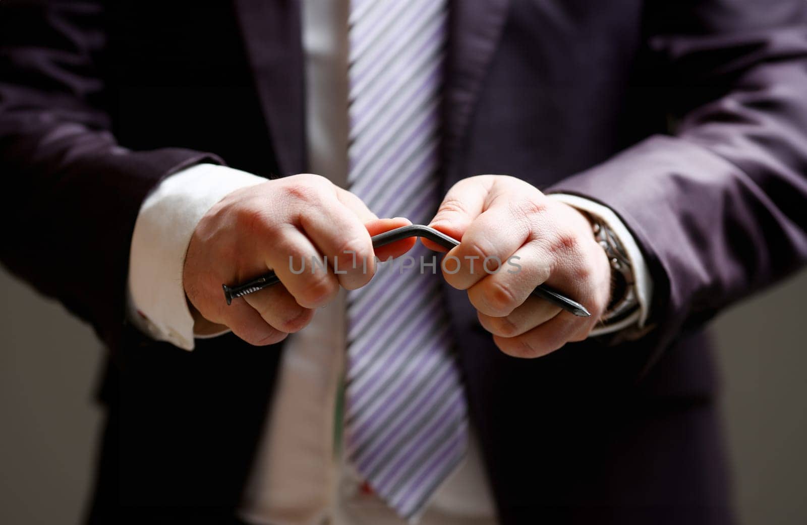 Man in suit and tie bend nail with arms closeup no limit energy easy problem solve issue superman help pressure concept