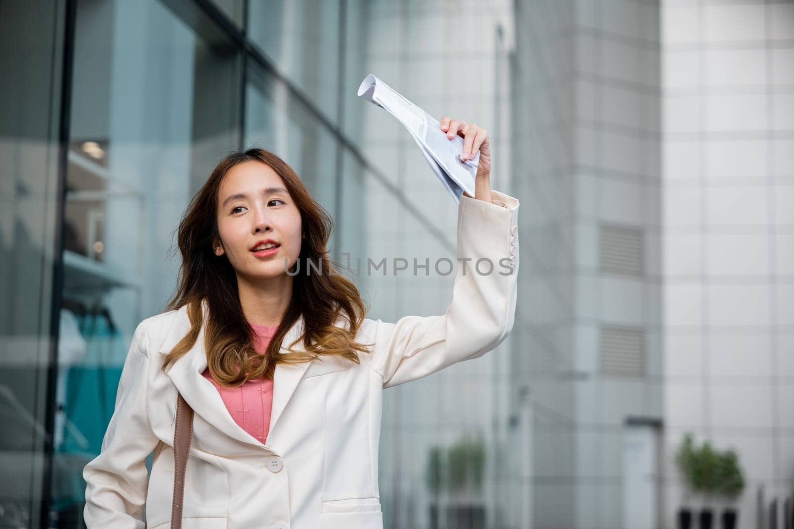 Businesswoman walking out the building after finish work shade sun UV with newspaper. Portrait of Young Asian woman wearing white shirt while cover the sun by news paper on the streets of downtown