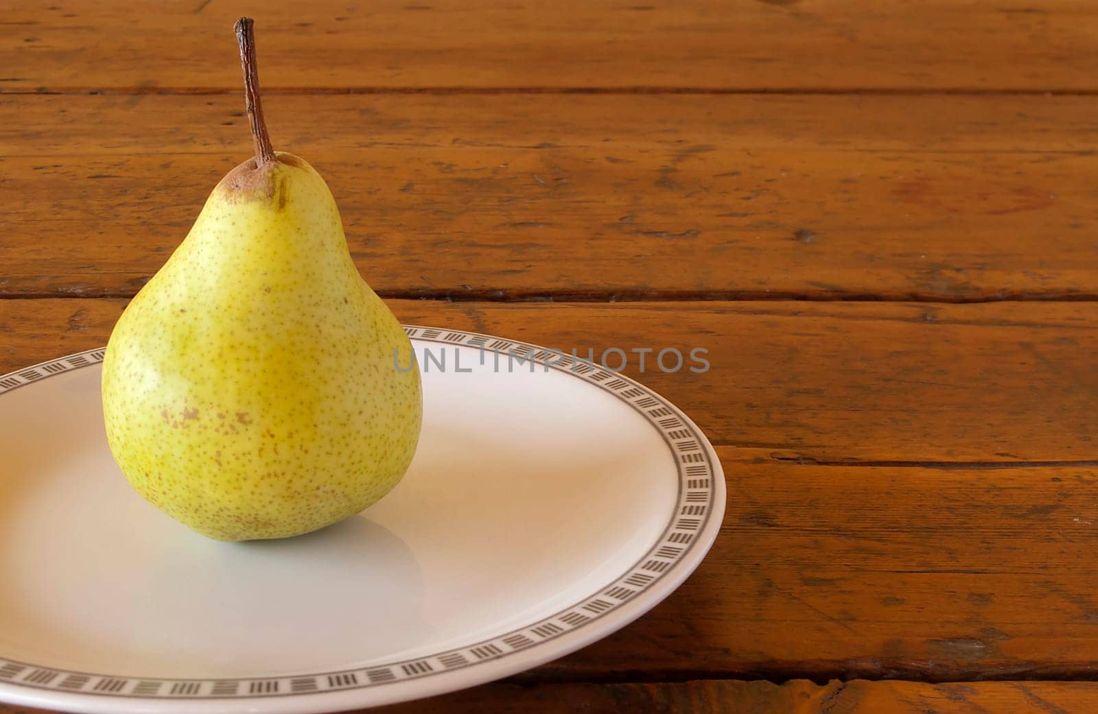one pear on white plate posed on old wood table