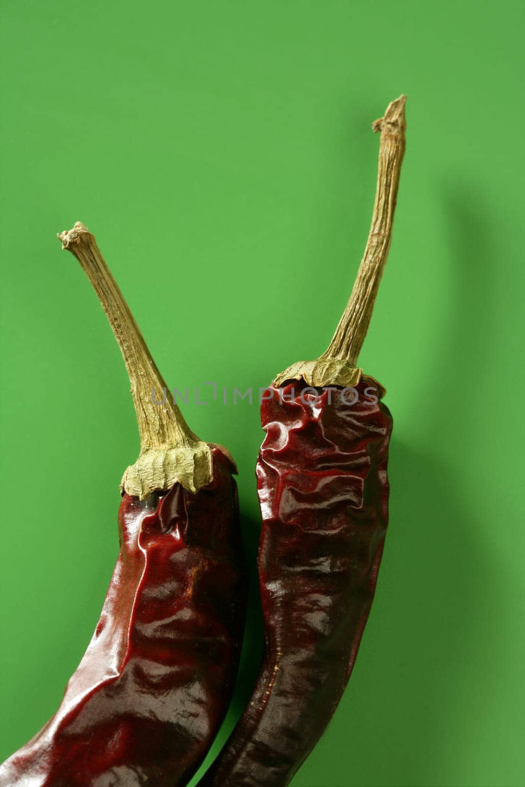 Two dried pepper, chili , over vivid studio green background