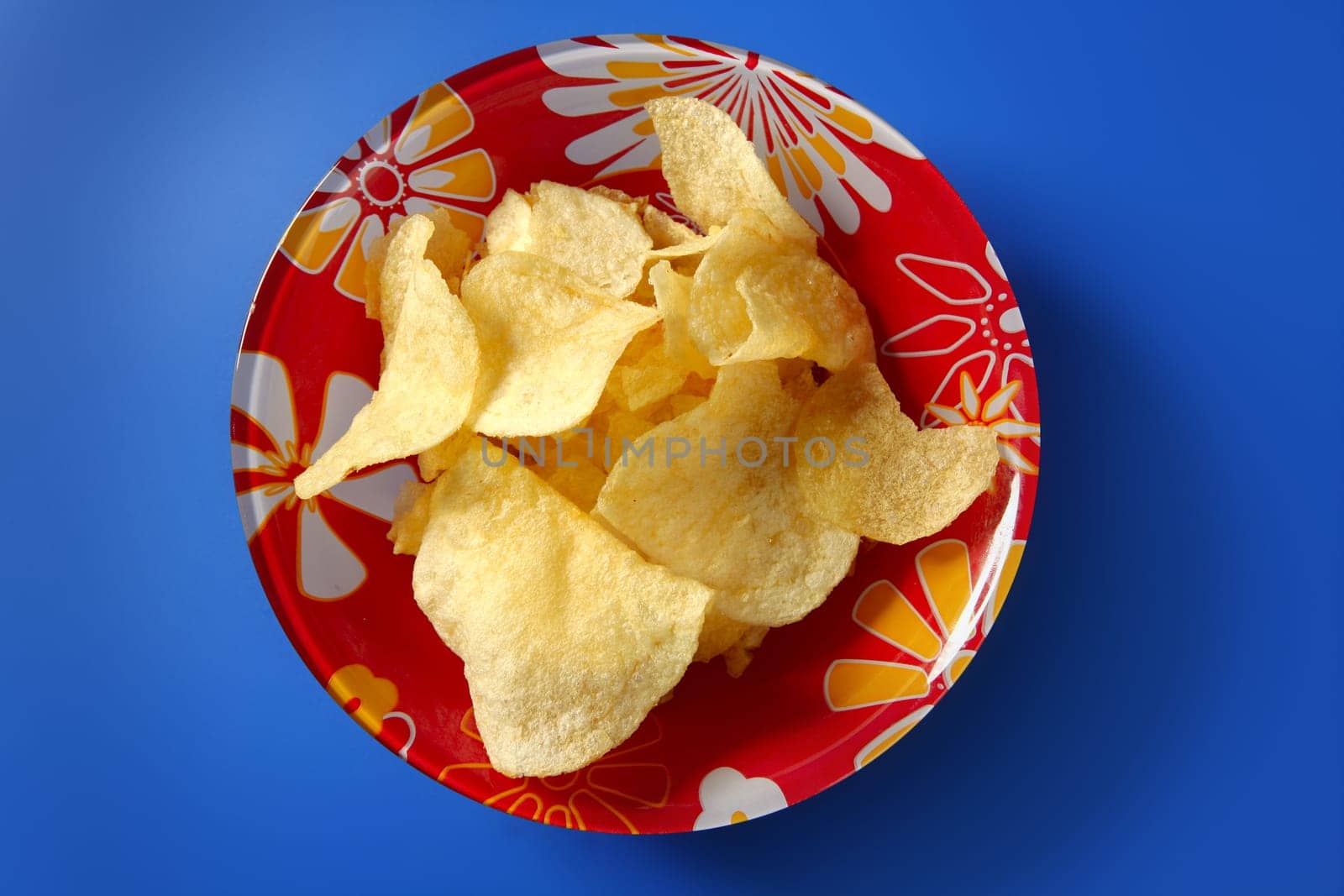 Potato fried chips on red plate over blue background