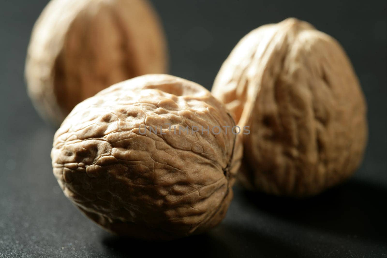Three walnuts with shells over black background and shadows