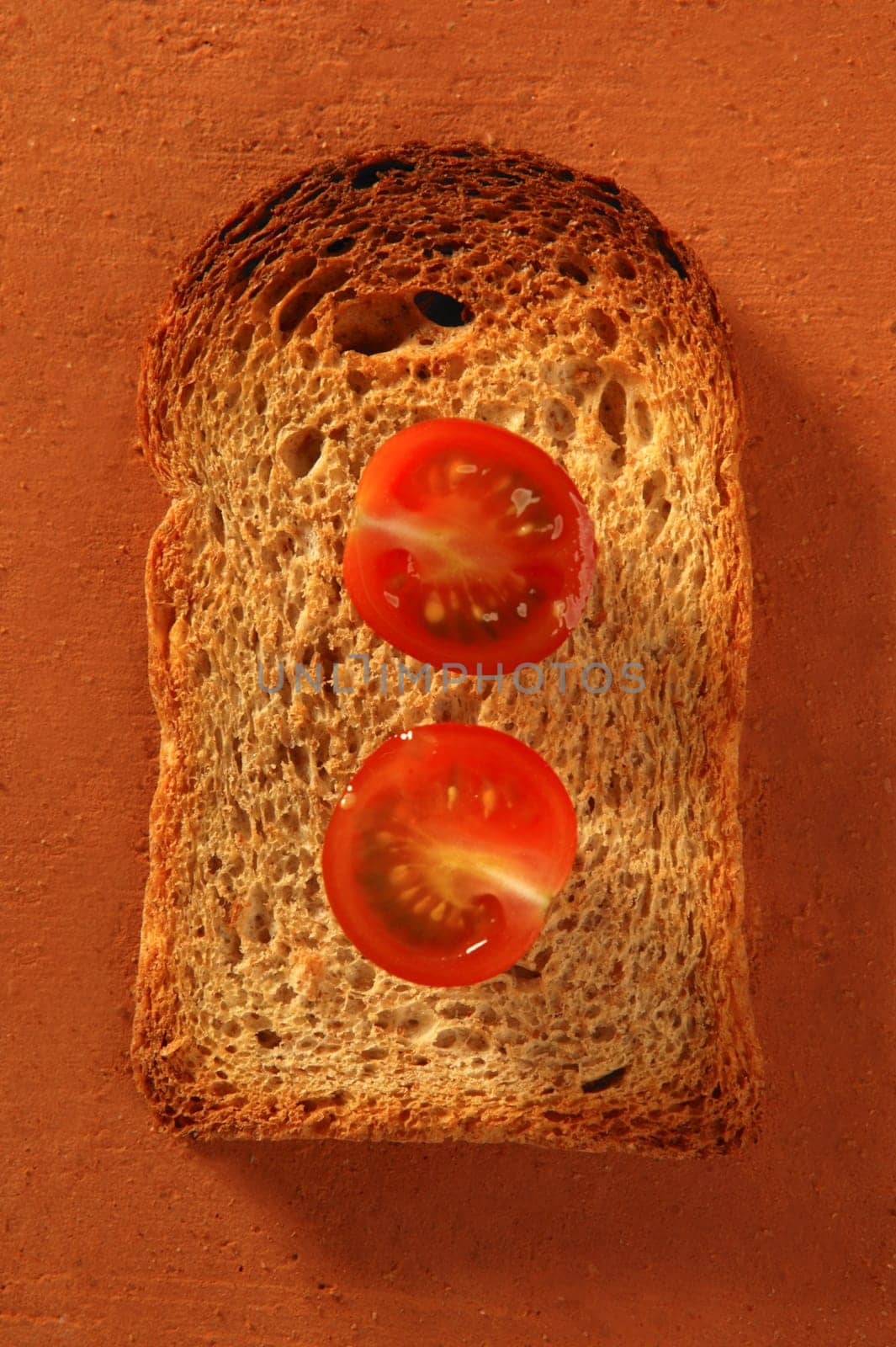 Toasted bread slices and cherry tomatoes on orange clay background