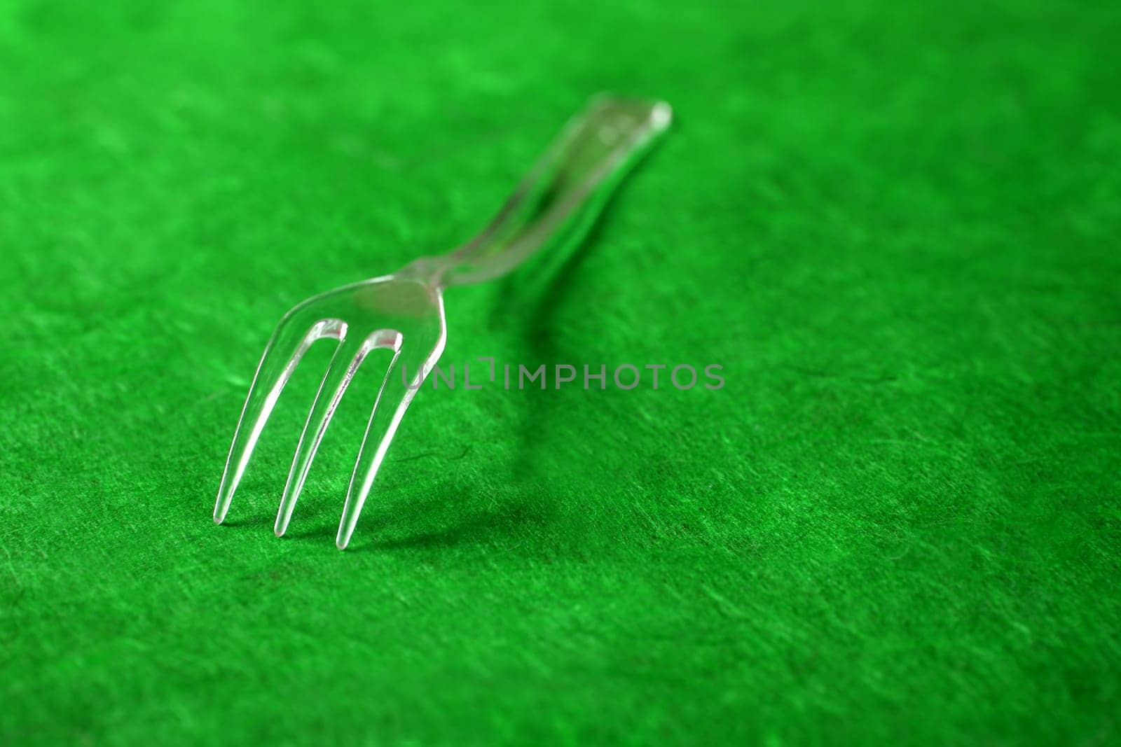 Transparent plastic fork on a textured vivid green background