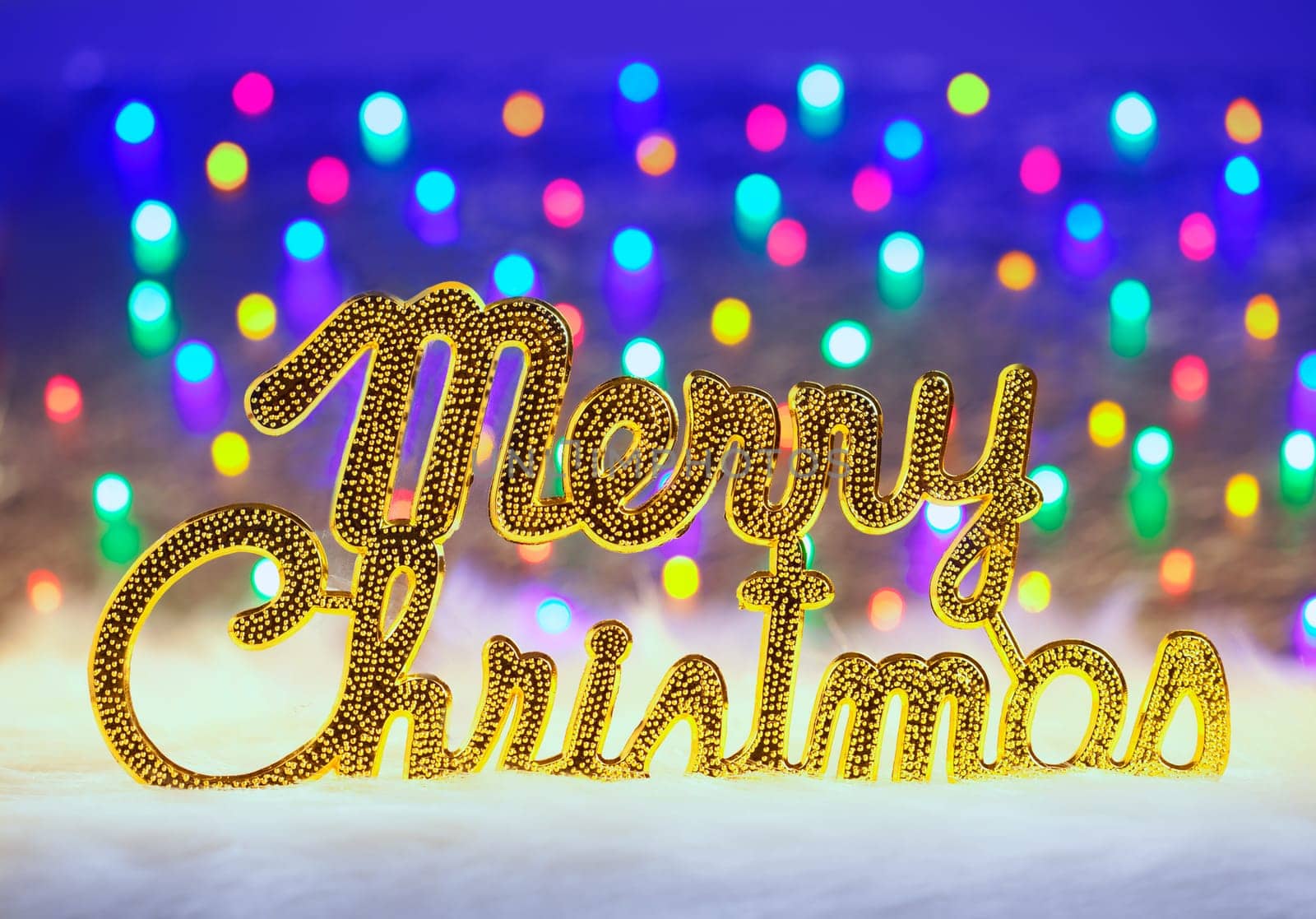 Merry christmas written in gold with colorful glowing lights