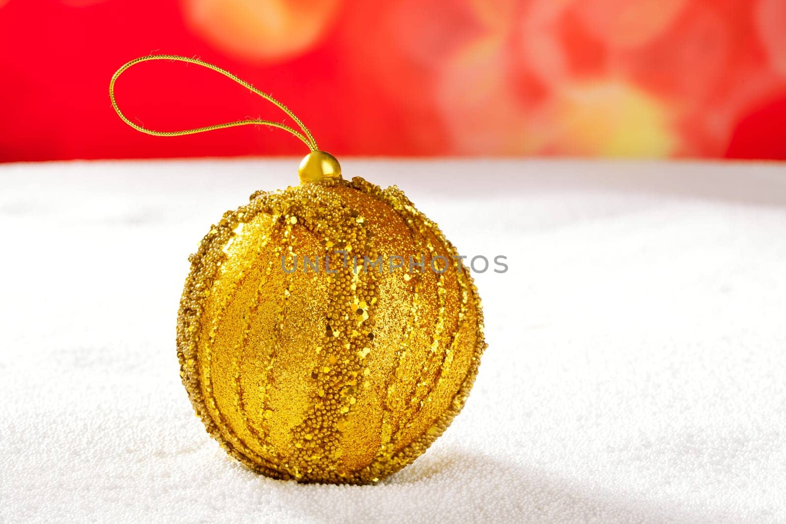 Christmas golden bauble on snow and red background
