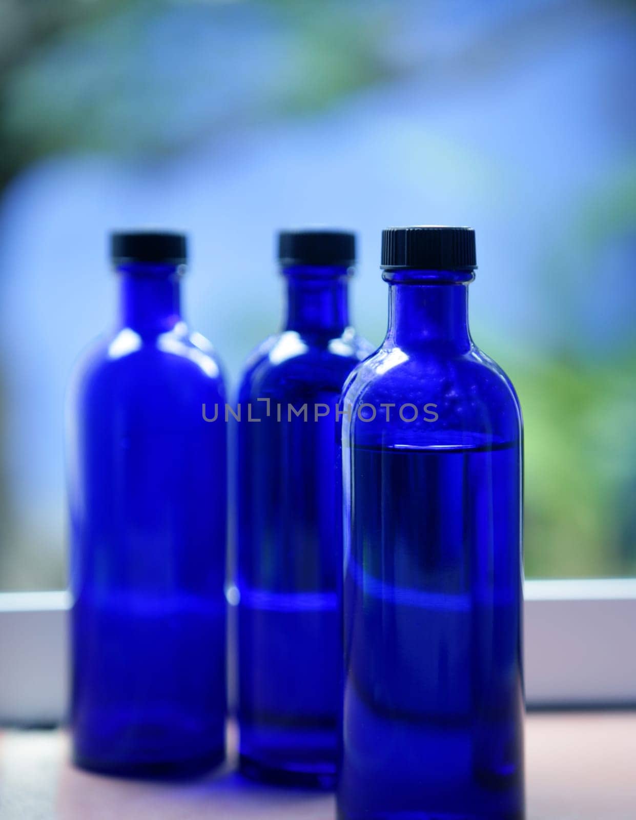 Three Blue glass body oil bottles in bathroom window