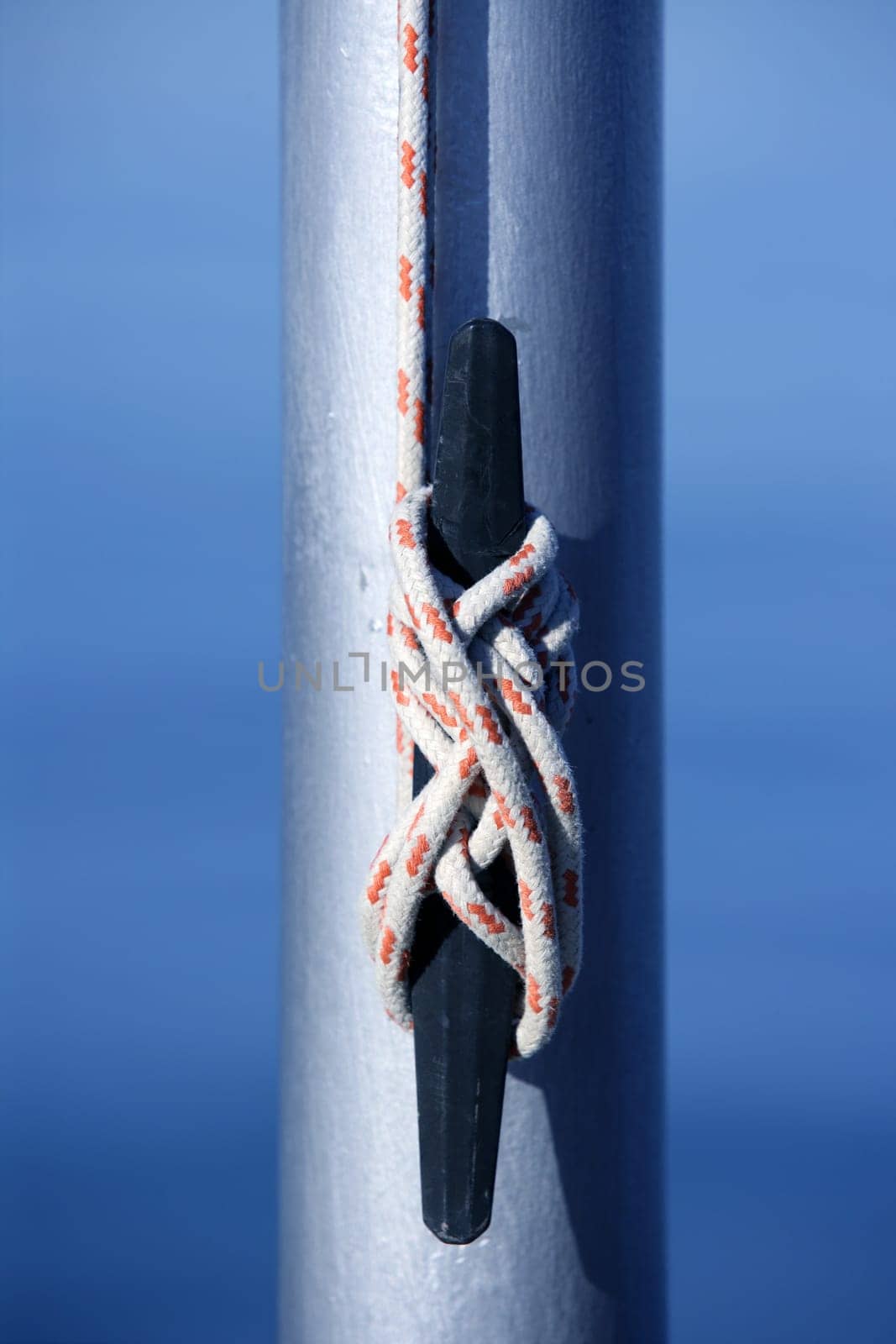 Marine rope, knot arround a steel pole, blue water background