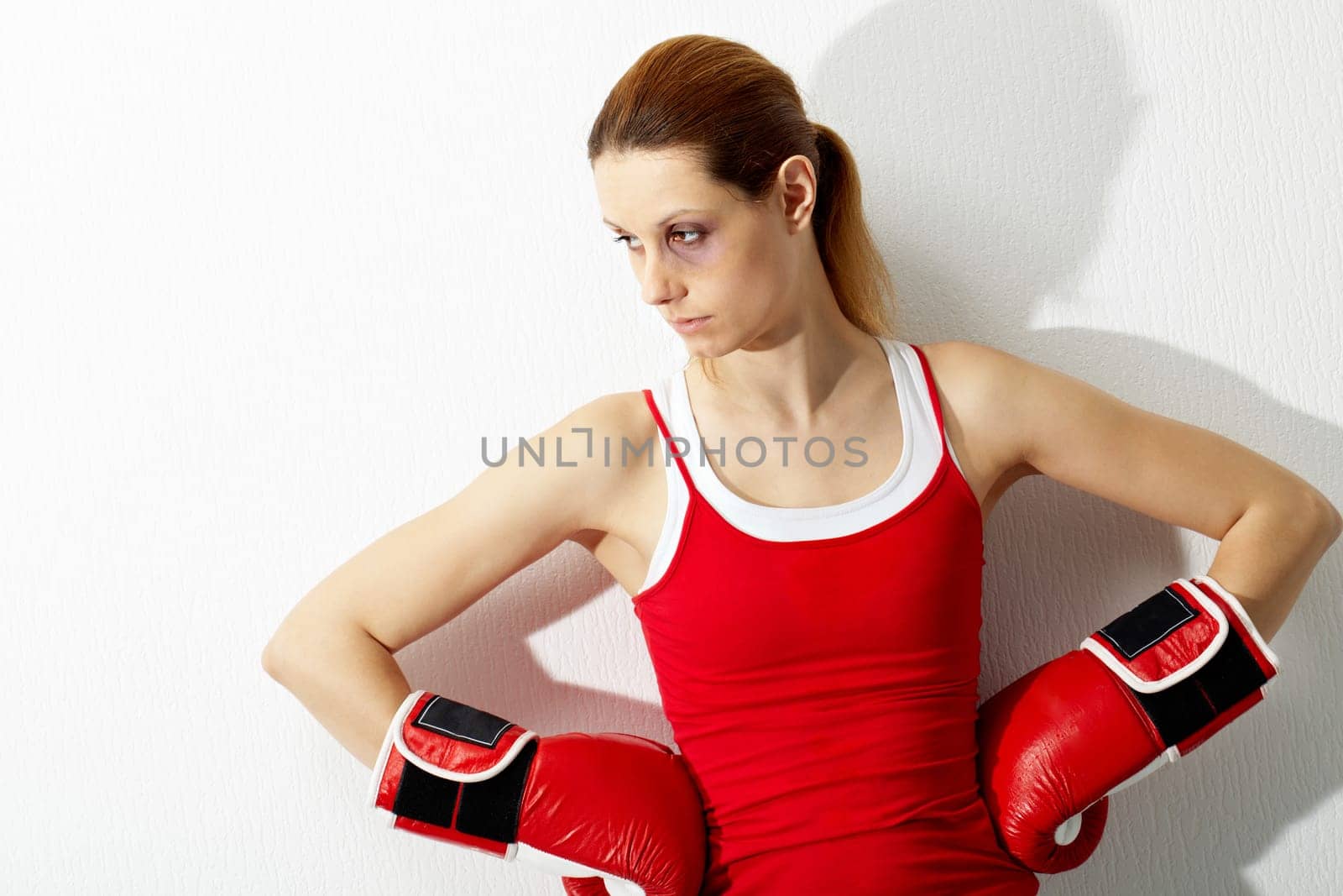 Portrait of young woman with bruise in red boxing gloves looking aside