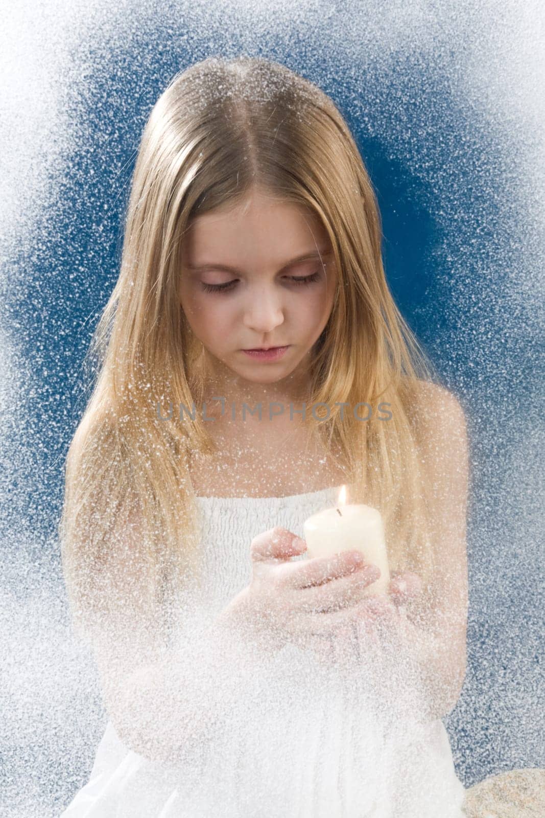 Image of praying girl looking at burning candle in her hands behind frosty window