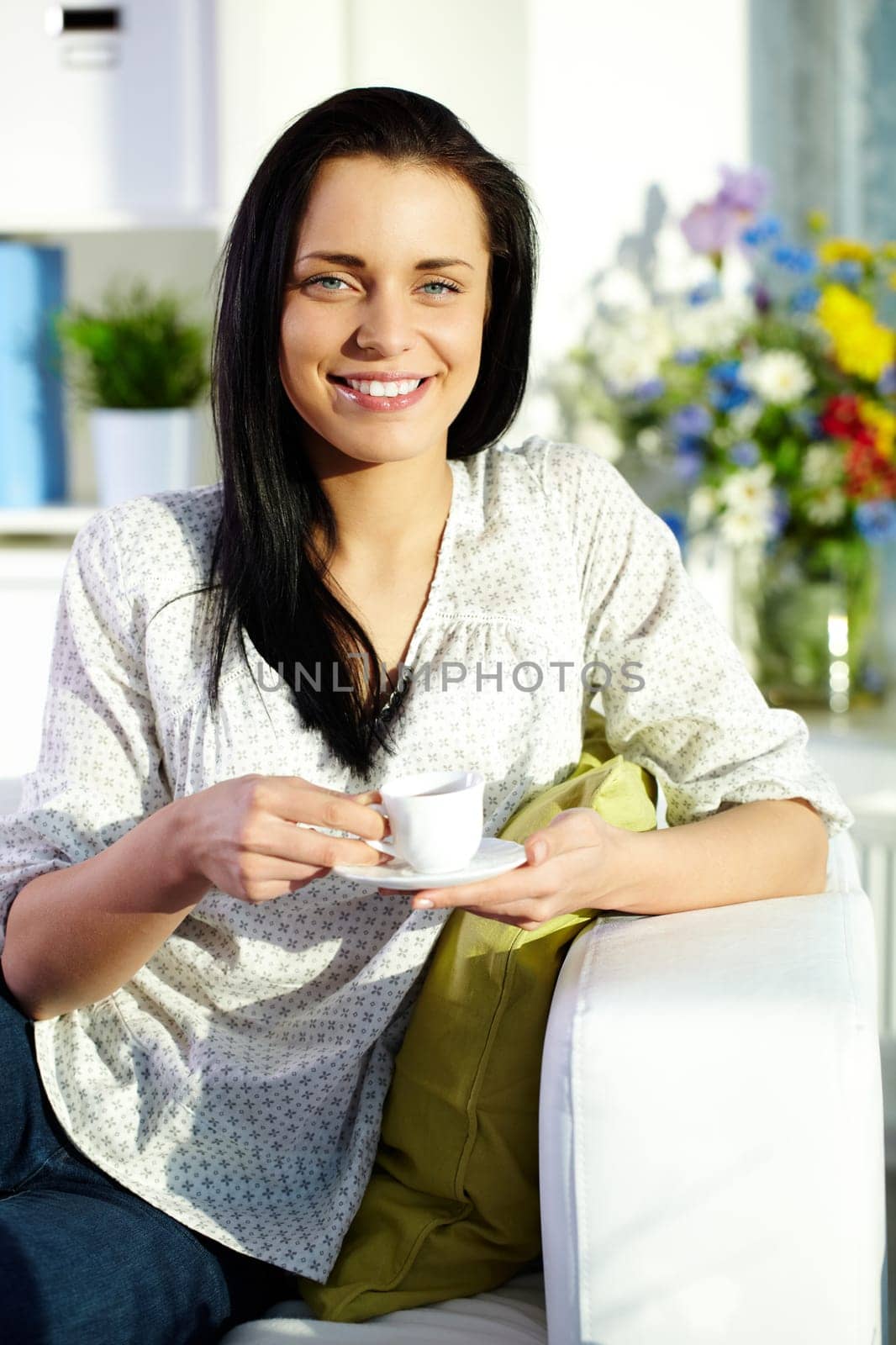 Portrait of brunette with cup of tea sitting on sofa and looking at camera