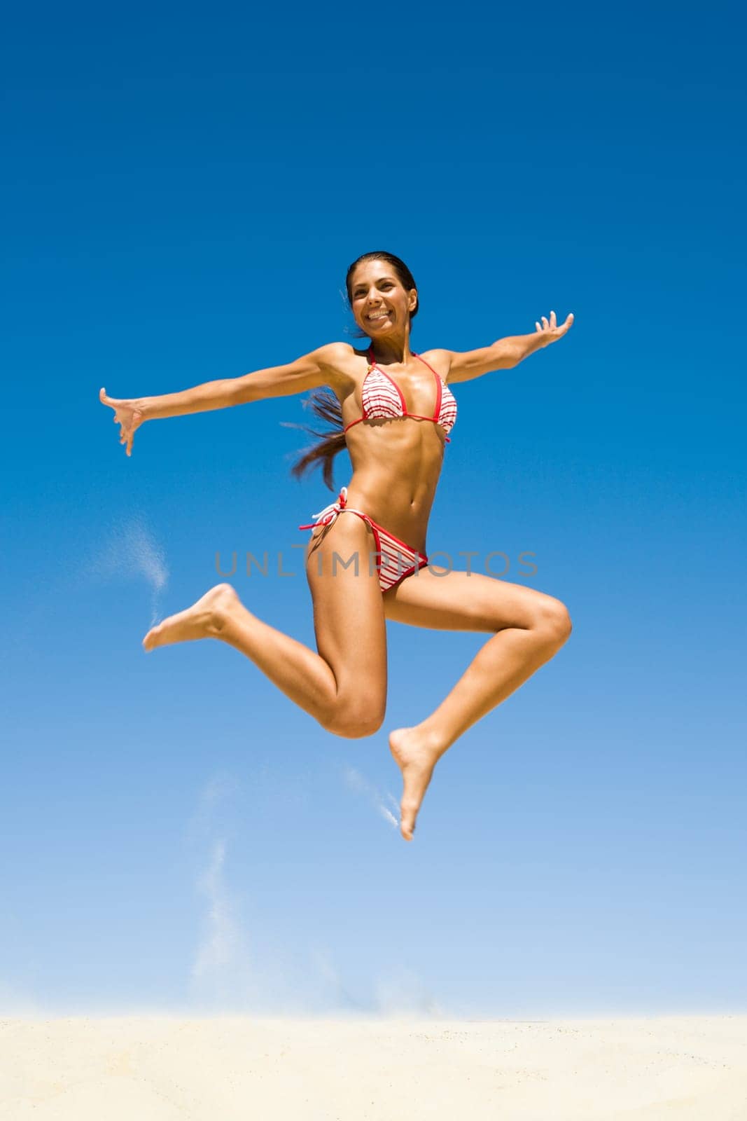 Photo of young happy girl leaping over sandy beach on the background of bright sky