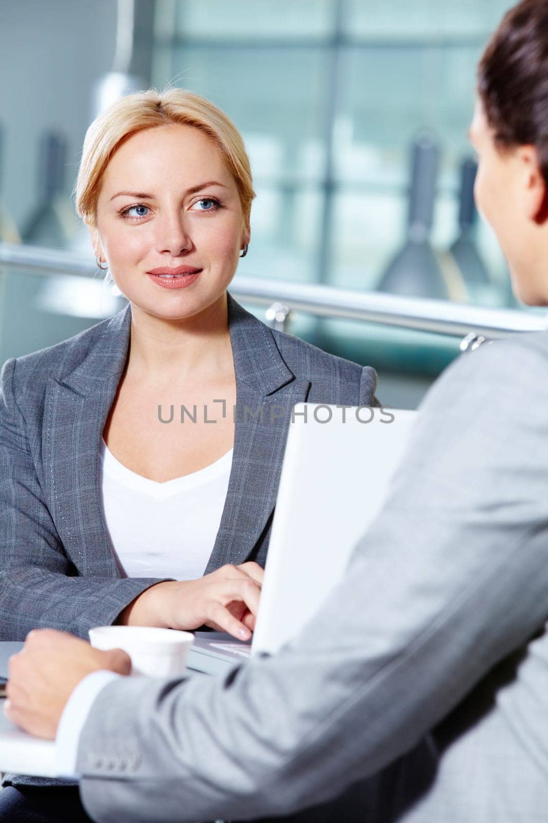 Portrait of pretty woman at workplace touching keys of laptop while speaking to man