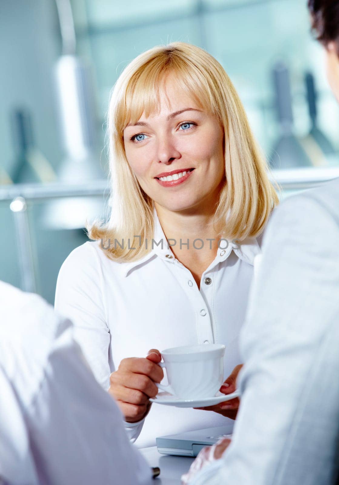 Portrait of pretty woman at workplace with coffee cup speaking to colleagues