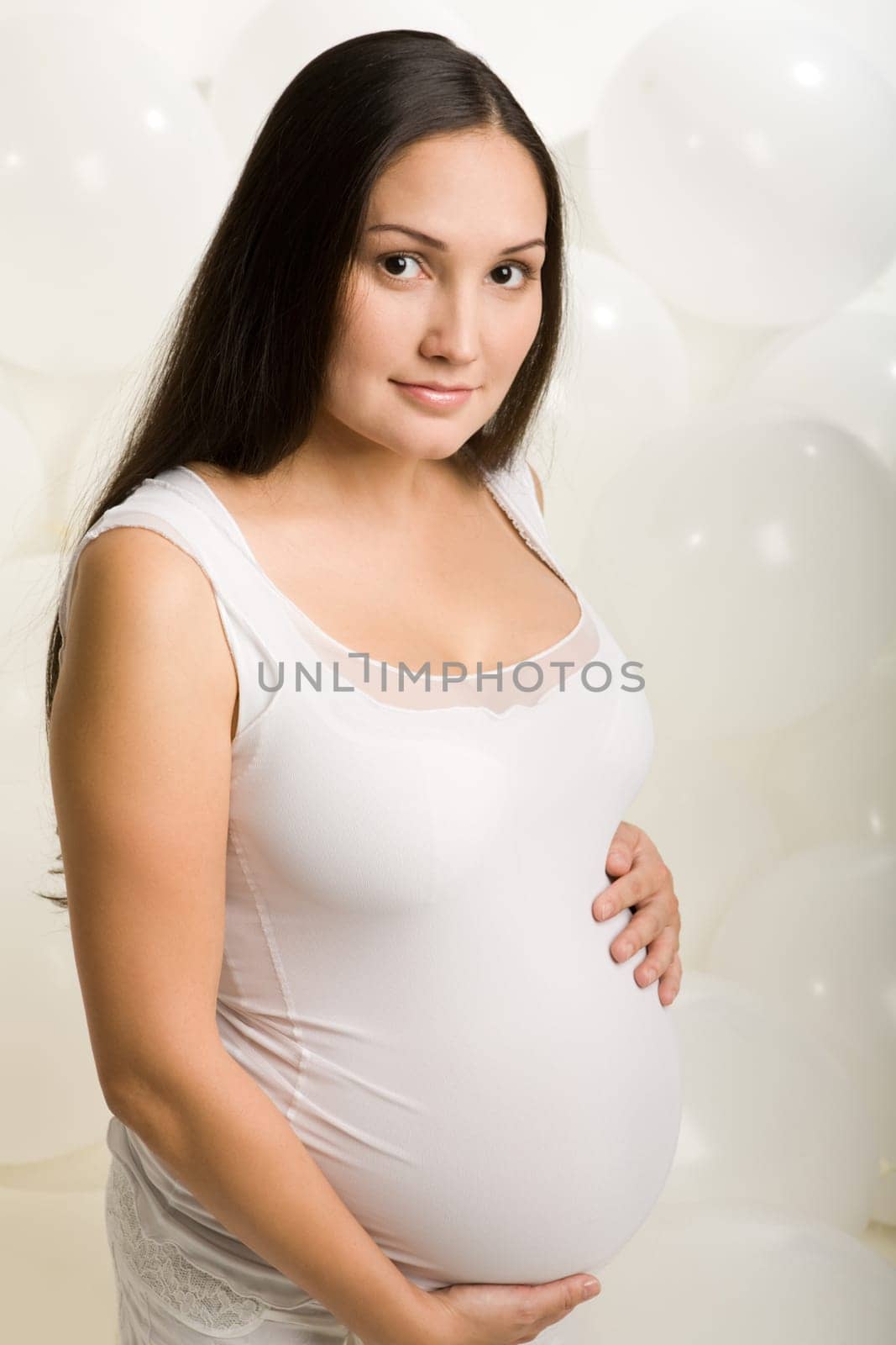 Portrait of pretty pregnant woman wearing white clothing on background of white balloons