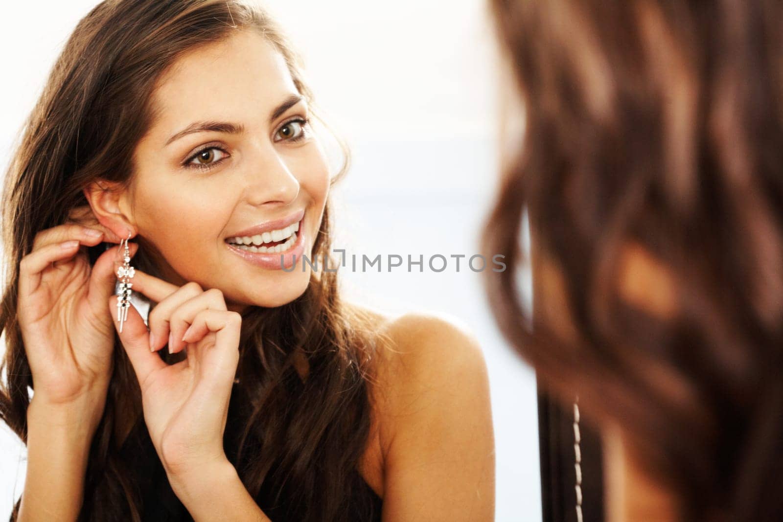 Image of pretty female looking in mirror and putting on earrings