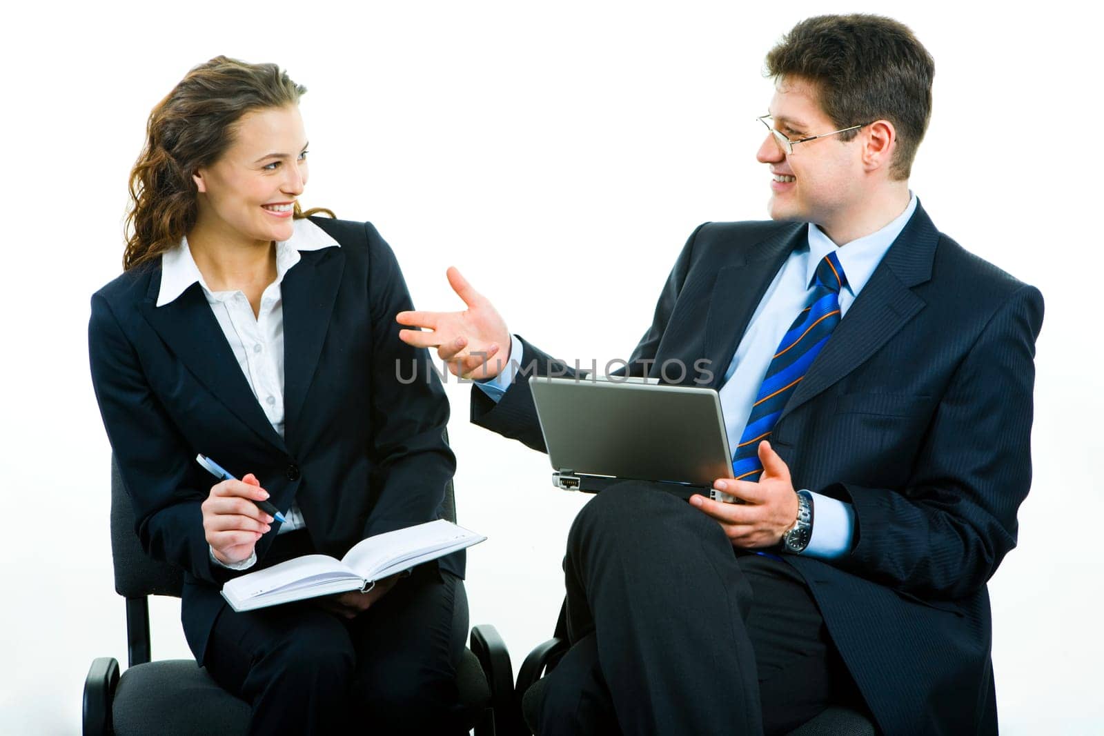 Portrait of two successful business partners sitting and looking at each other with smiles at meeting: man with laptop, woman holding pen and notebook