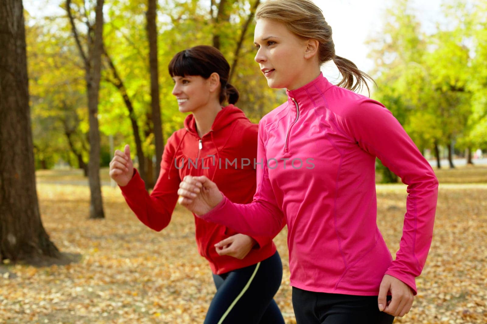 Two young women jogging in autumn park