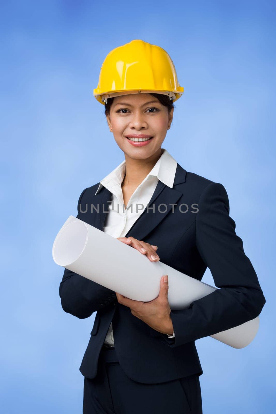 Portrait of pretty female with paper in hands and helmet on head looking at camera over blue background
