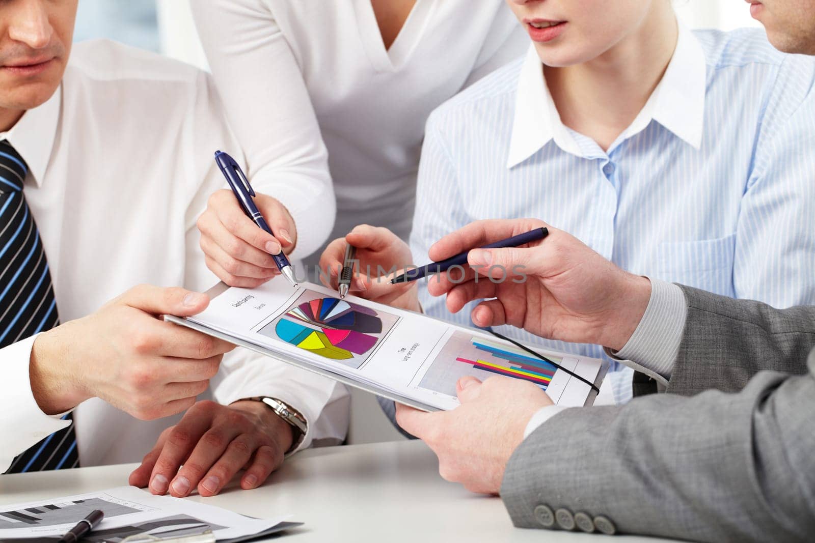 Image of several hands of working partners discussing business charts