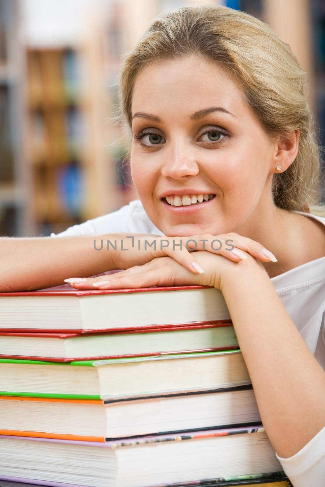 Portrait of pretty student putting her chin on hand over pile of books