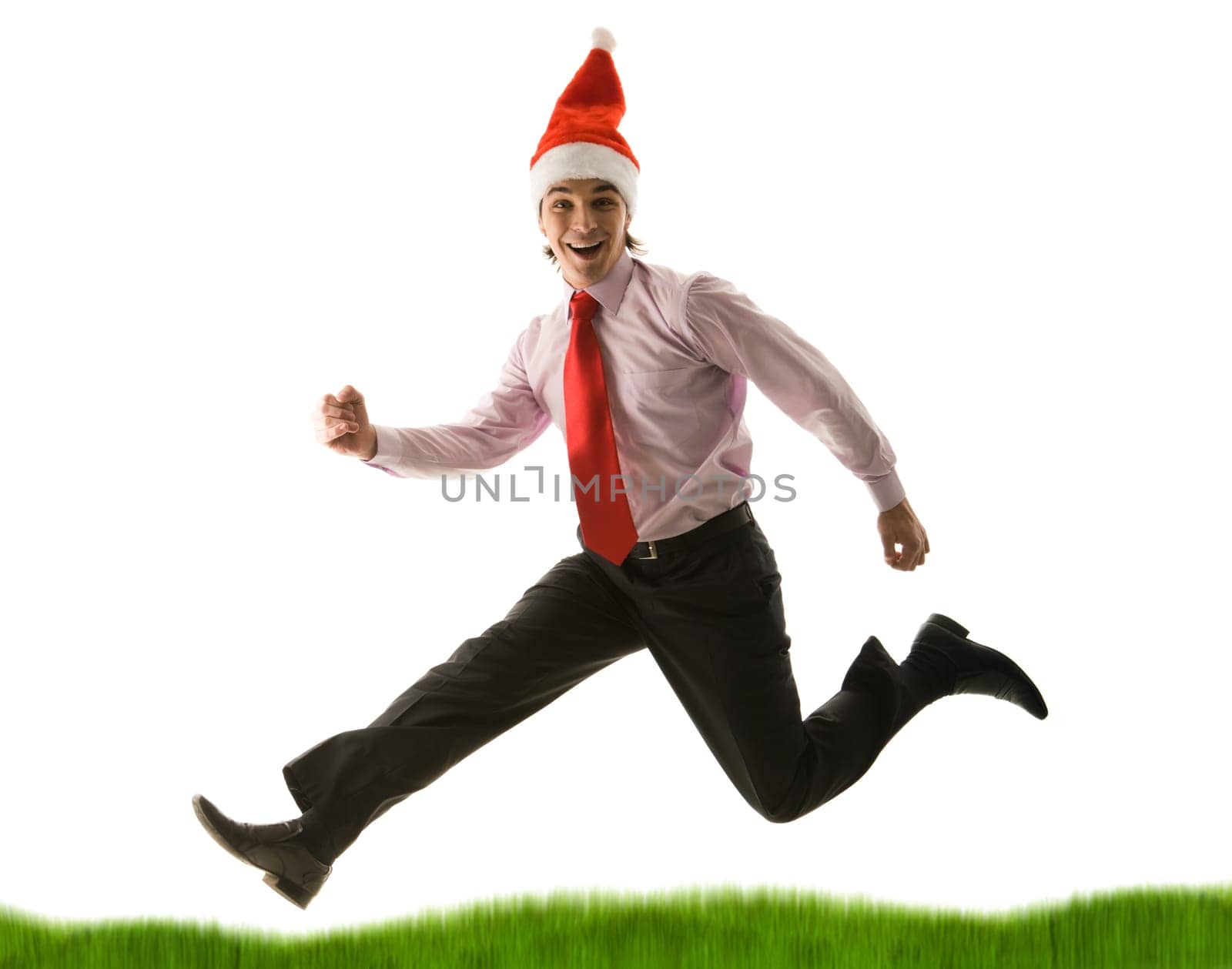 Portrait of businessman in santa cap running down green grass on white background