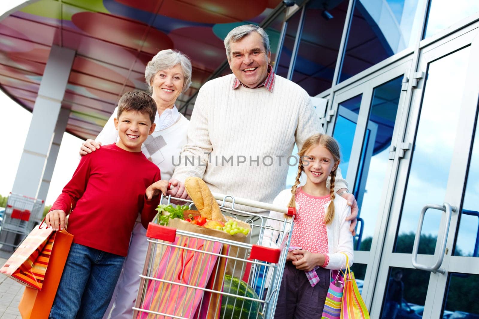Portrait of happy grandparents and grandchildren with package of food near supermarket