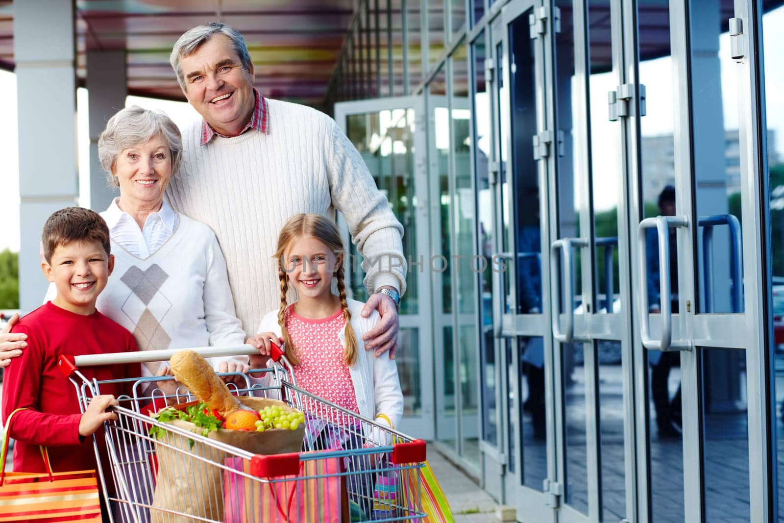 Portrait of happy grandparents and grandchildren with package of food near supermarket