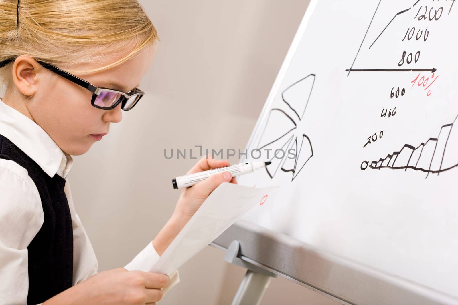 Portrait of smart girl with pen in hand standing by whiteboard