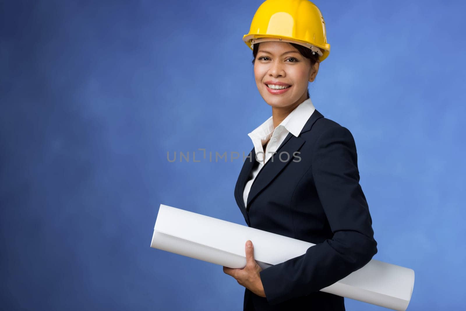 Portrait of pretty female with blueprints in hands and helmet on head smiling