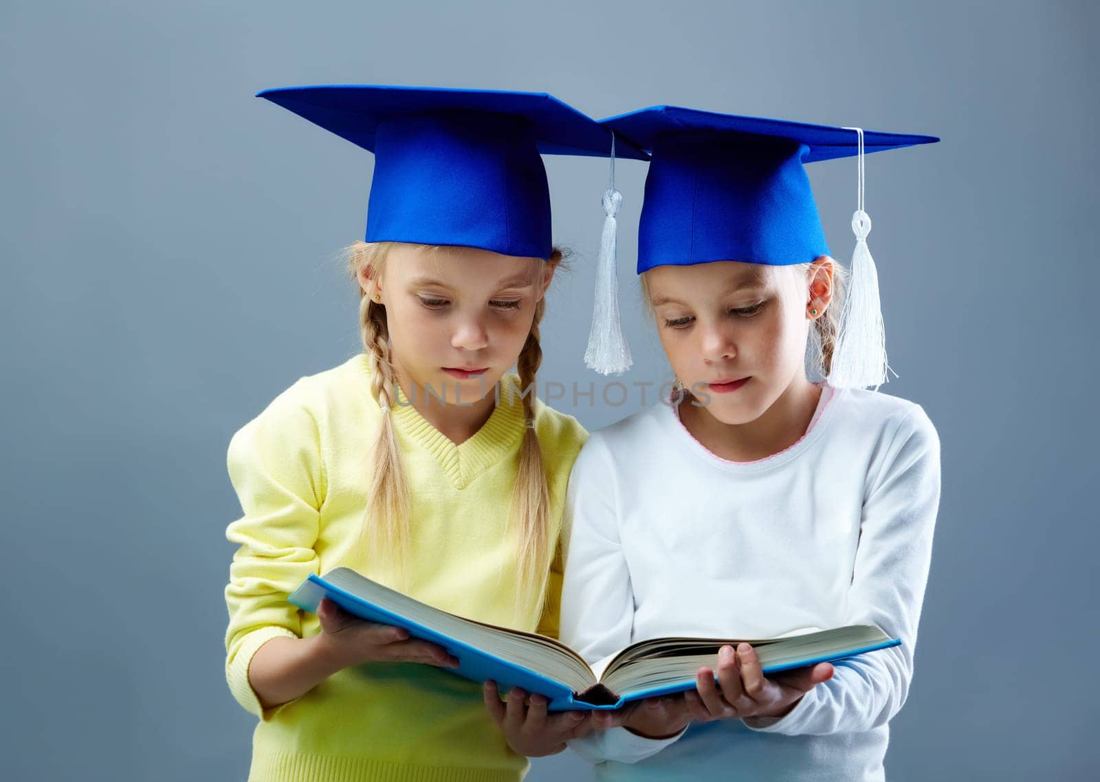 Portrait of lovely twin girls in hats with tassels reading book