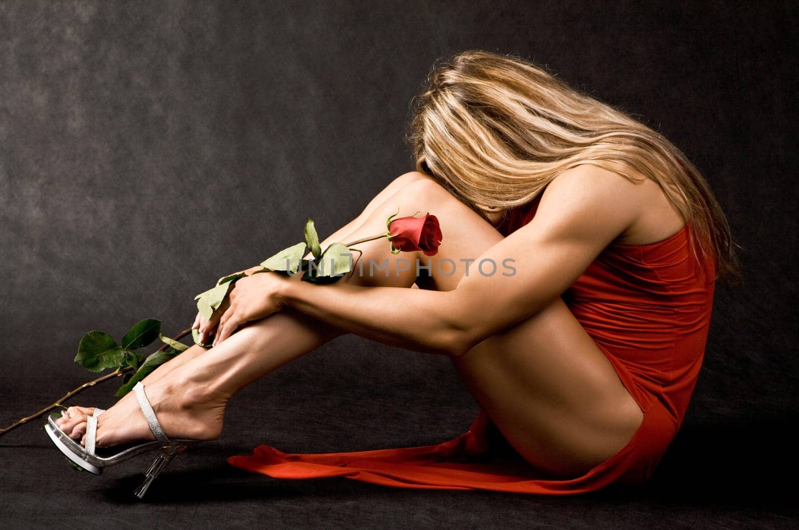 Portrait of strong female sitting with red rose in hand on black background