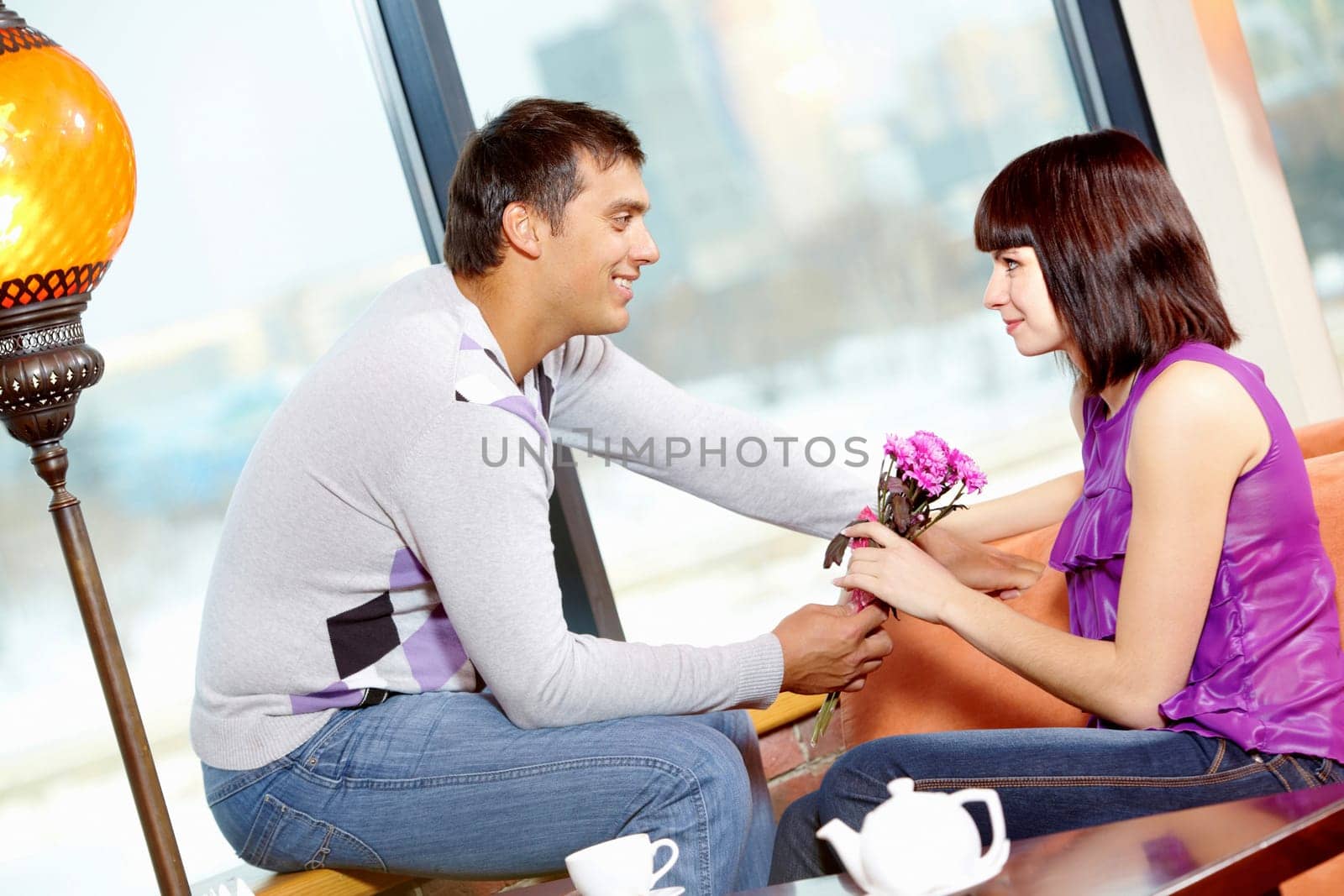 Happy man giving bunch of flowers to young female in cafe