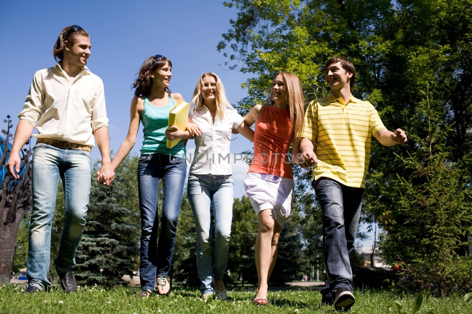 Photo of cheerful friends walking down green grass in park and chatting