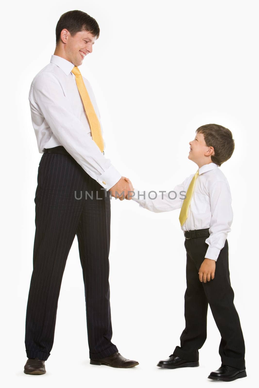 Portrait of father and son standing and handshaking while looking at each other on white background