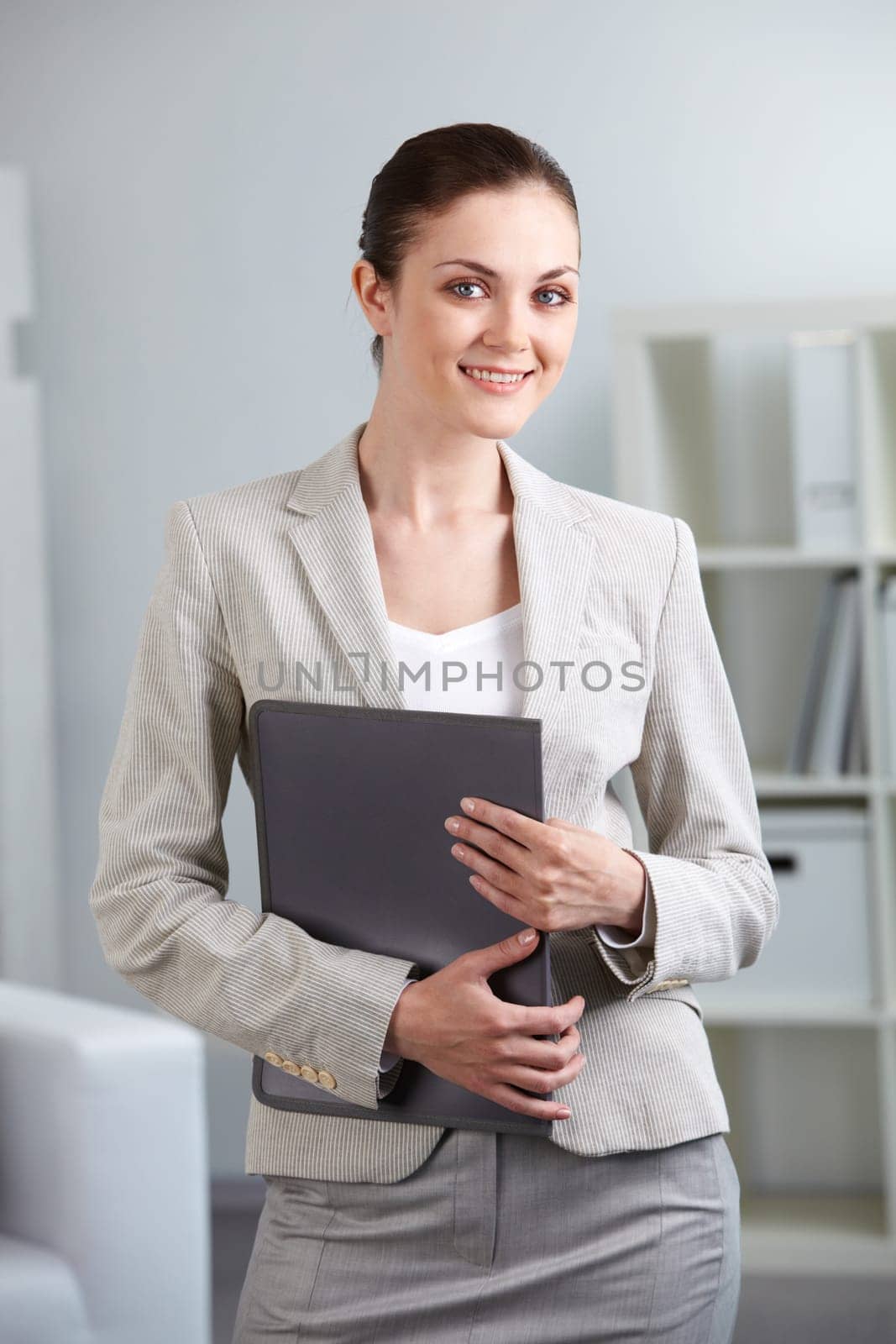 Portrait of smiling businesswoman with folder looking at camera in office