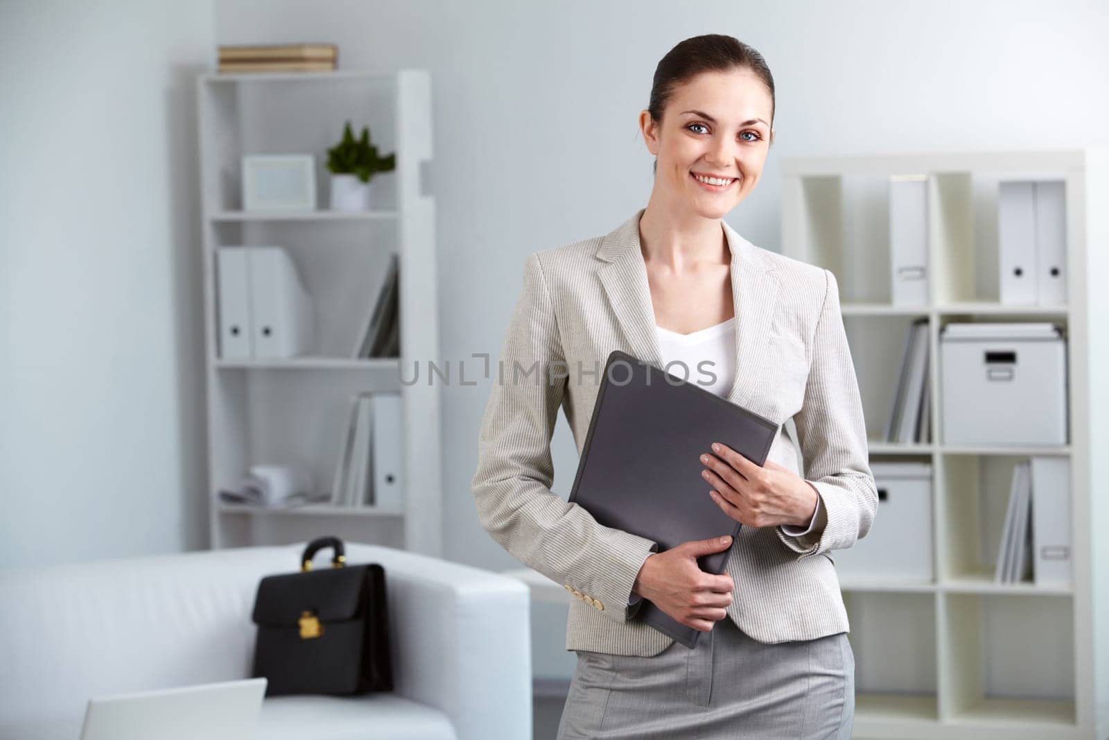 Portrait of smiling businesswoman with folder looking at camera in office
