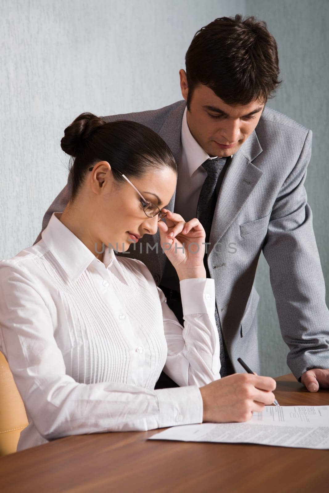 Businesswoman reads a contract with the pen in her hand and man in the gray suit is near