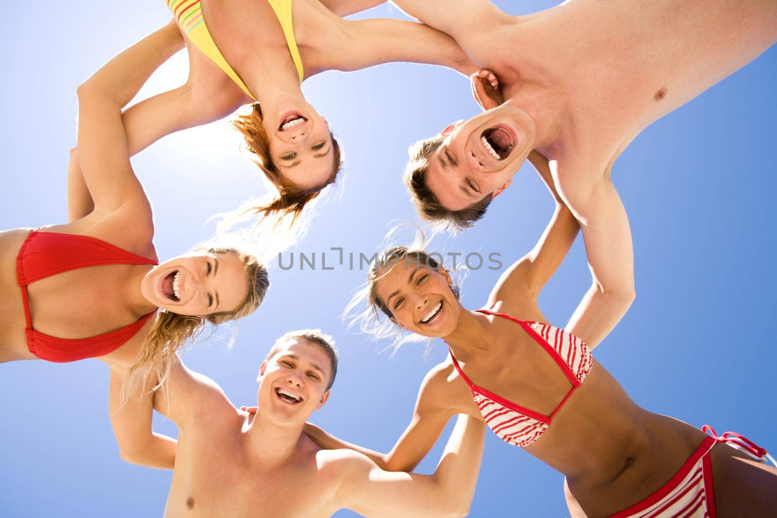 Several happy friends embracing each other and looking at camera on background of blue sky at summer