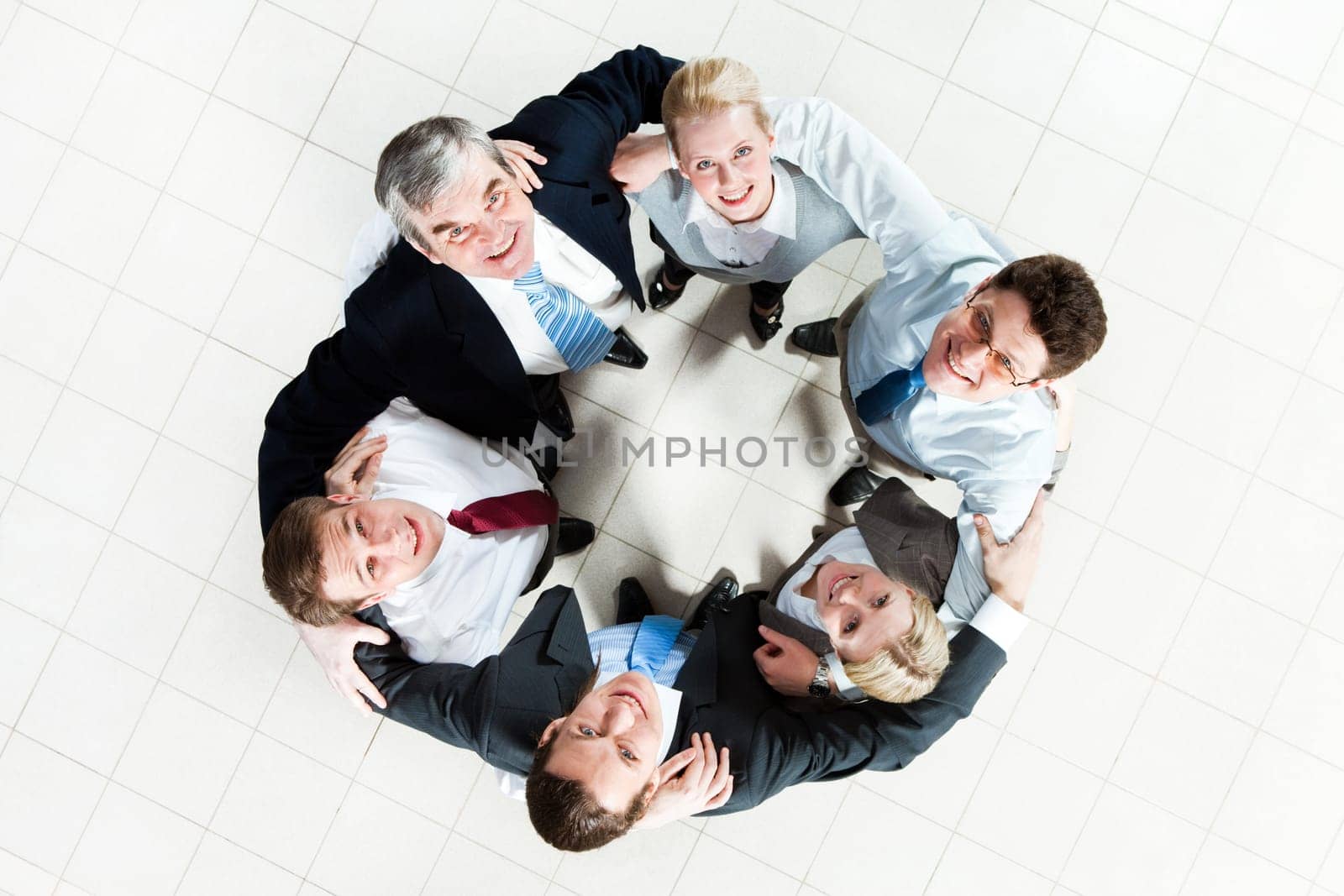 Above view of several business partners looking upwards at camera while embracing each other