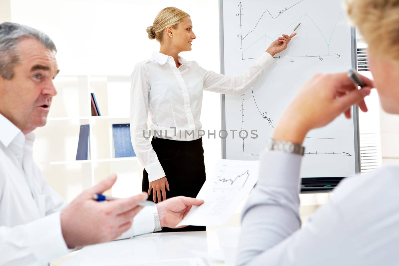 Image of successful businesswoman standing by whiteboard while her colleagues listening to her