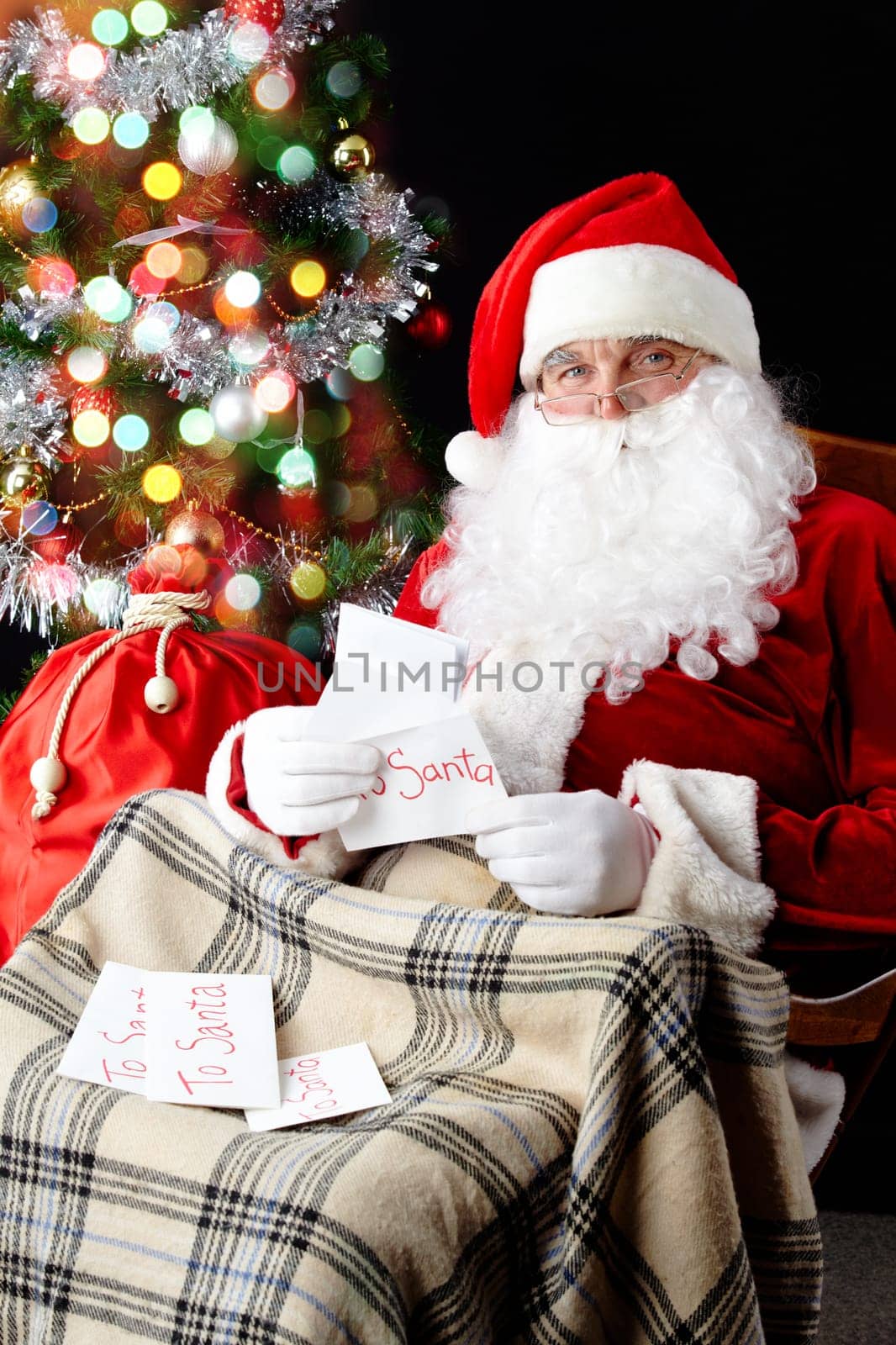 Santa sitting at the Christmas tree and reading Christmas letters