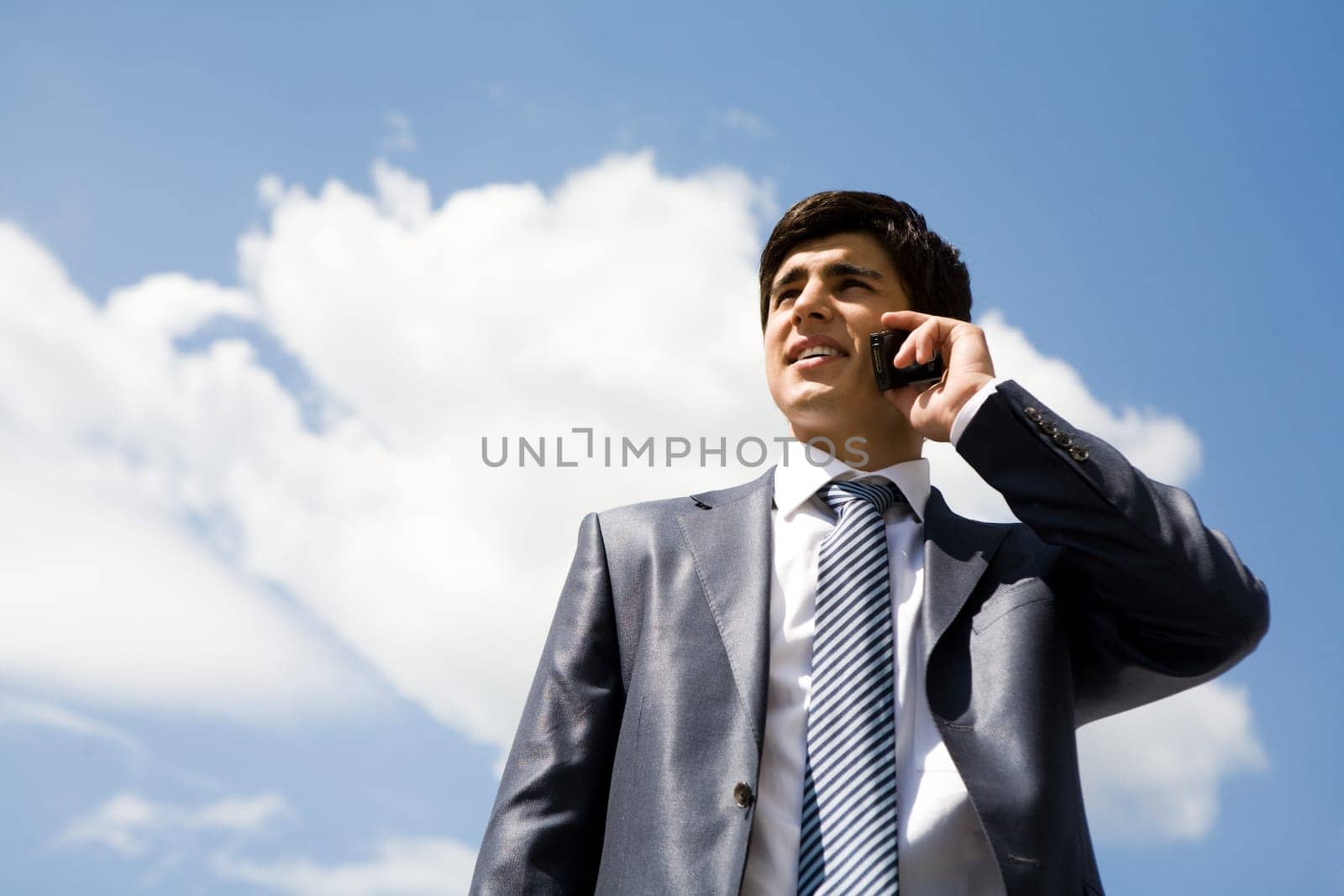 Portrait of confident businessman calling by cellular phone against cloudy sky