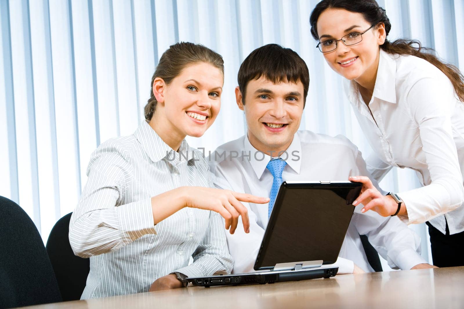 Team of three businesspeople gathered around the table with laptop and working