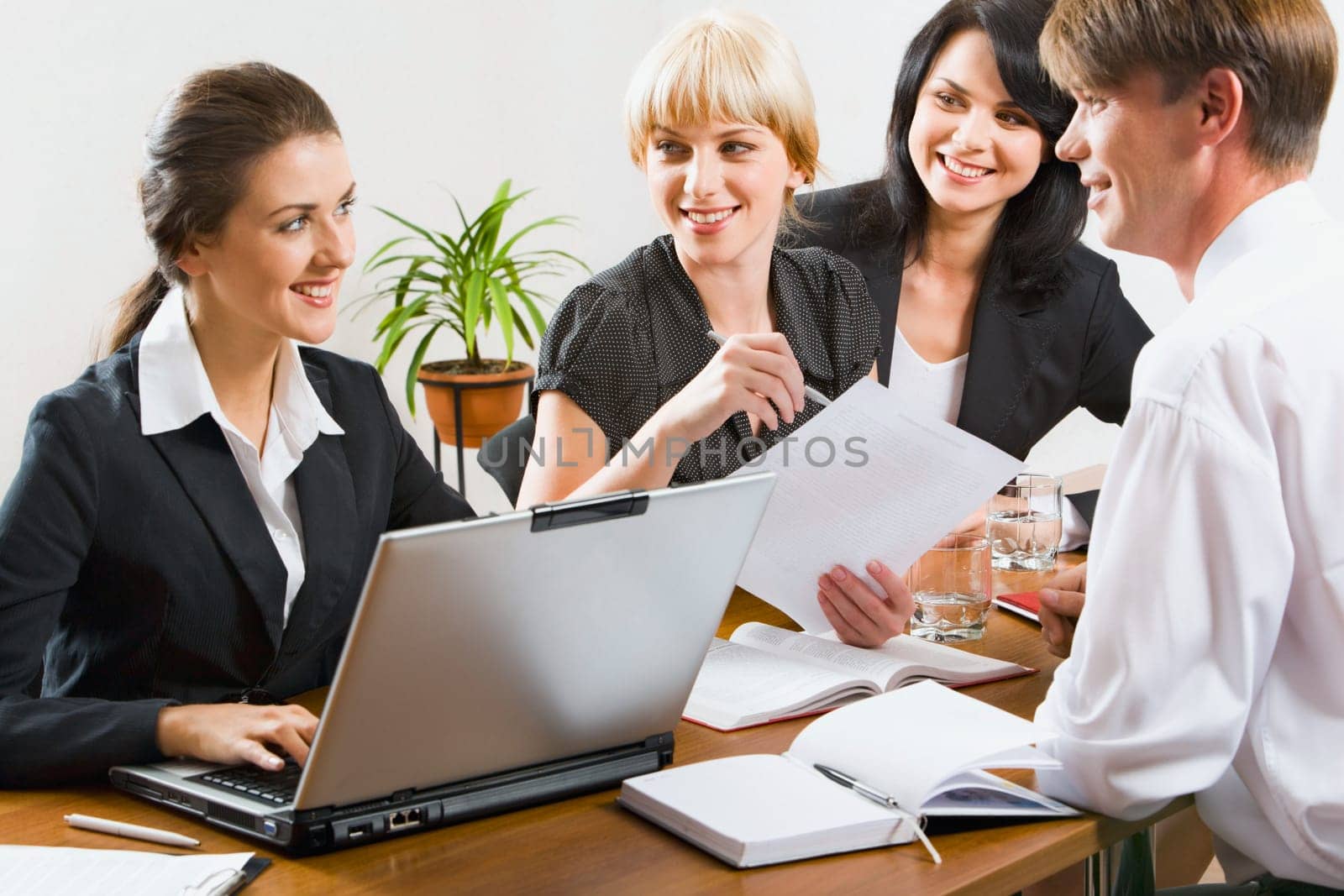 Group of successful business people sitting at the table with laptop, notepads, papers, pen and glasses on it discussing an important questions
